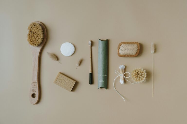 A flat lay image showing various zero-waste essentials: a reusable coffee cup, a cloth shopping bag filled with unpackaged produce, bamboo utensils, a metal water bottle, and a small glass jar of homemade cleaning solution, all arranged on a natural wood surface.